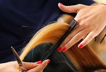 Female hairdresser hold in hand between fingers lock of blonde hair, comb and scissors closeup